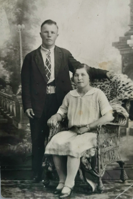 Vanha kuva, jossa nainen istuu tuolilla ja mies seisoo tuolin sivustalla.