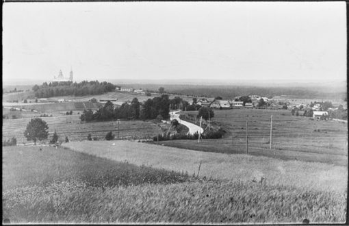 Vanha mustavalkoinen kuva pellosta ja kylästä.