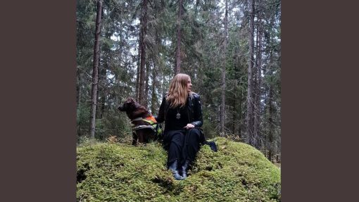 Nainen istuu metsässä vierellään koira.